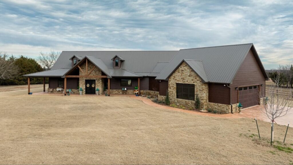 Ranch-style barndominium with brown TruLog steel siding, stone accents, and a metal roof.
