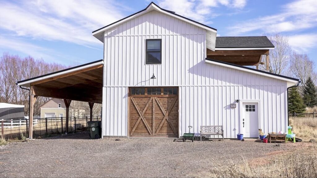 White barndominium with TruLog steel board and batten siding and wood barn doors.