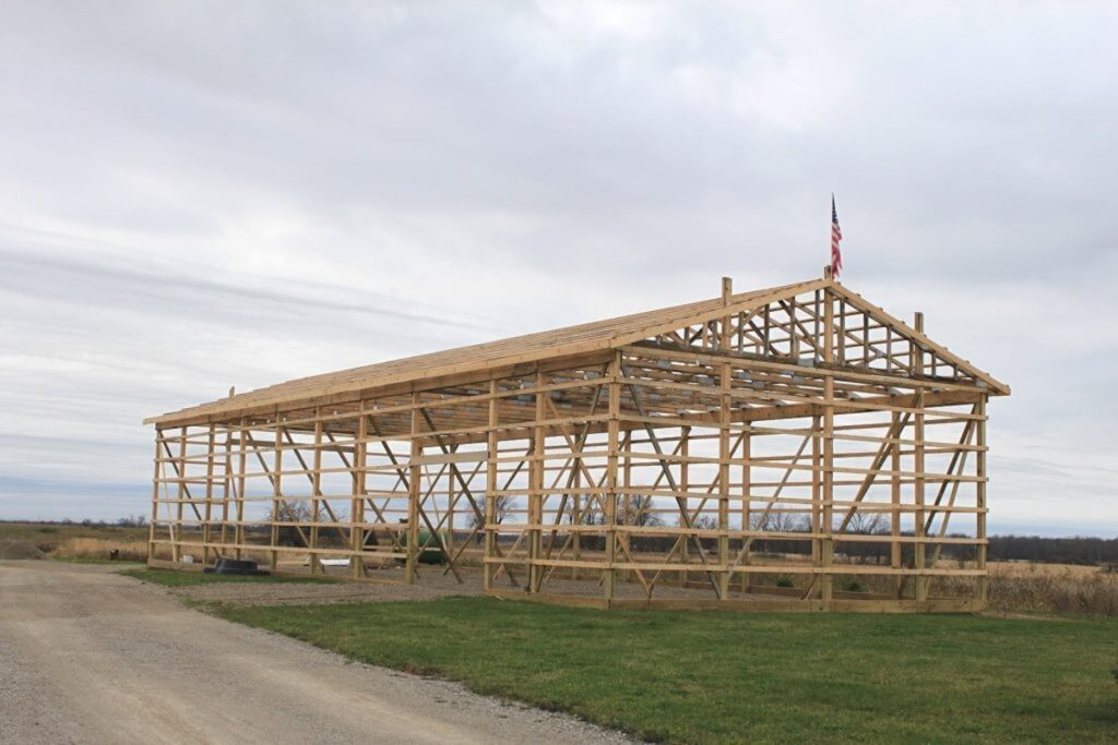 The wood post-and-beam frame of a large pole barn under construction, set against an overcast sky.