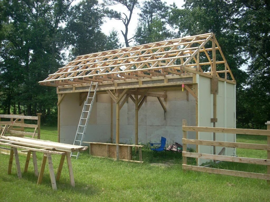 A small pole barn mid-build showing the open post frame, roof trusses, and partially-installed wall panels.
