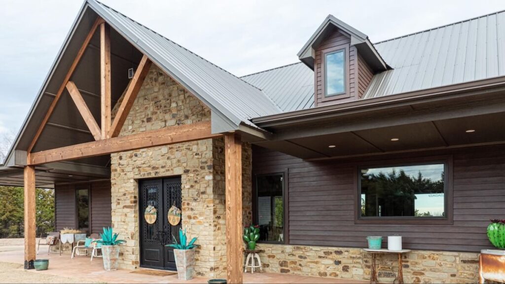 The front exterior of a home with a mix of stone, wood beams, and TruLog steel lap siding