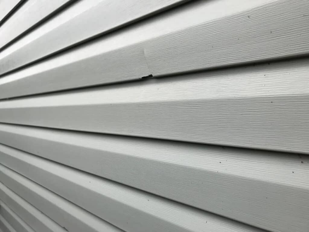 A closeup of damaged vinyl siding that looks like wood