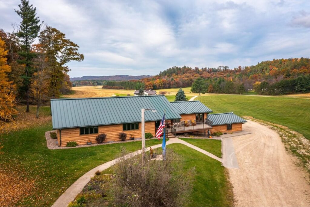 Aerial view of a ranch-style home with TruLog steel log siding and a green standing-seam metal roof on a rural property in autumn.