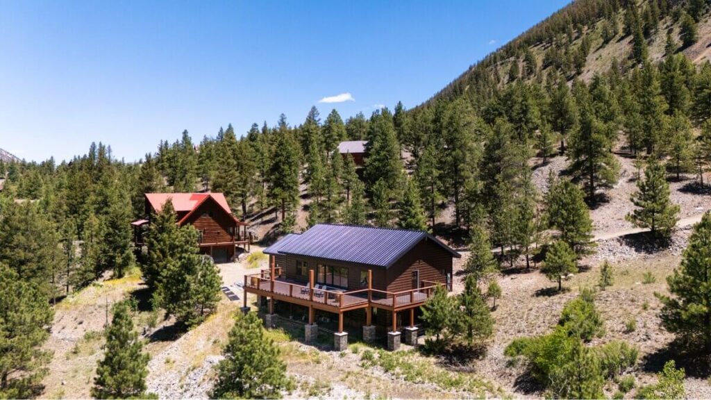 Aerial view of log cabins with TruLog steel siding and metal roofing nestled among pine trees on a mountainside.