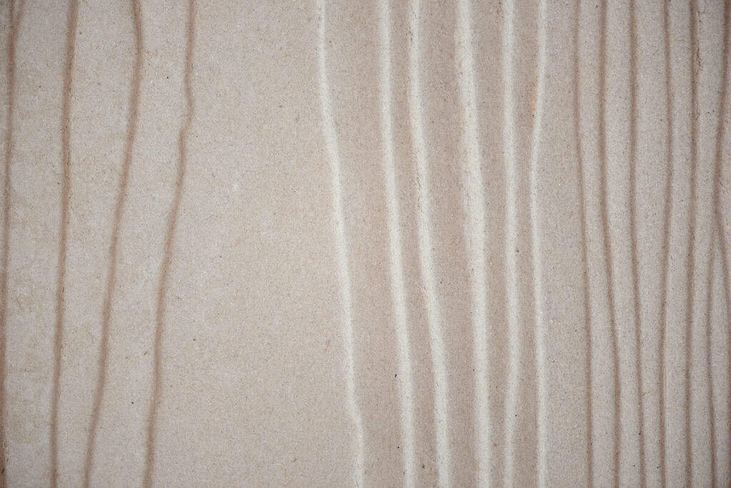 Close-up of light-colored fiber cement board showing pressed wood grain texture.