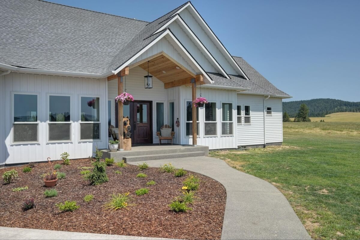 A modern farmhouse exterior with white TruLog steel board and batten siding, a shingle roof, and a covered entryway.