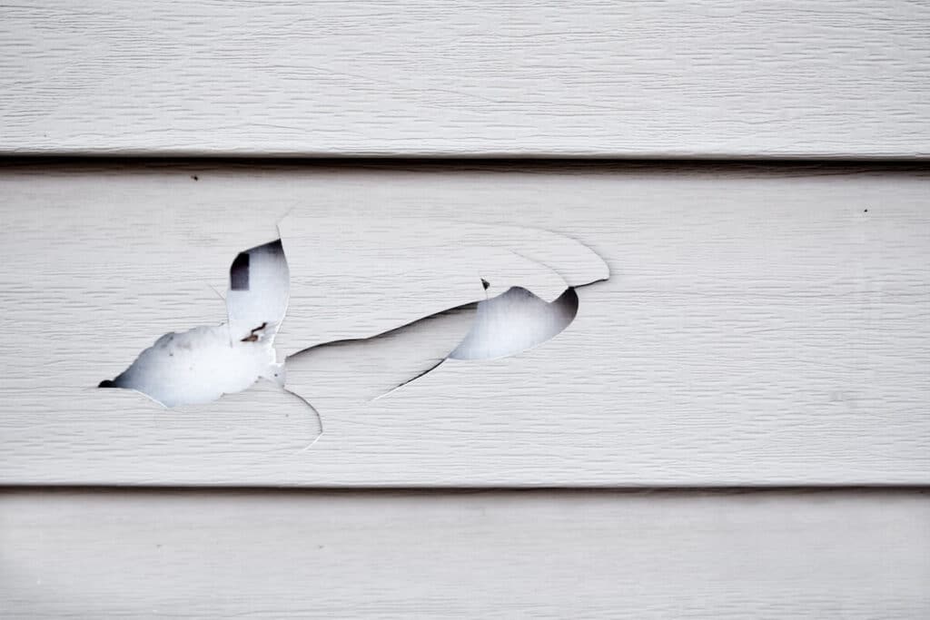 A closeup of vinyl siding with cracks and holes