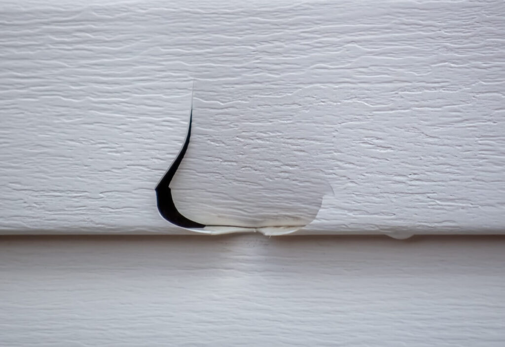 A closeup of damaged vinyl siding, which isn't a strong hail-resistant siding option