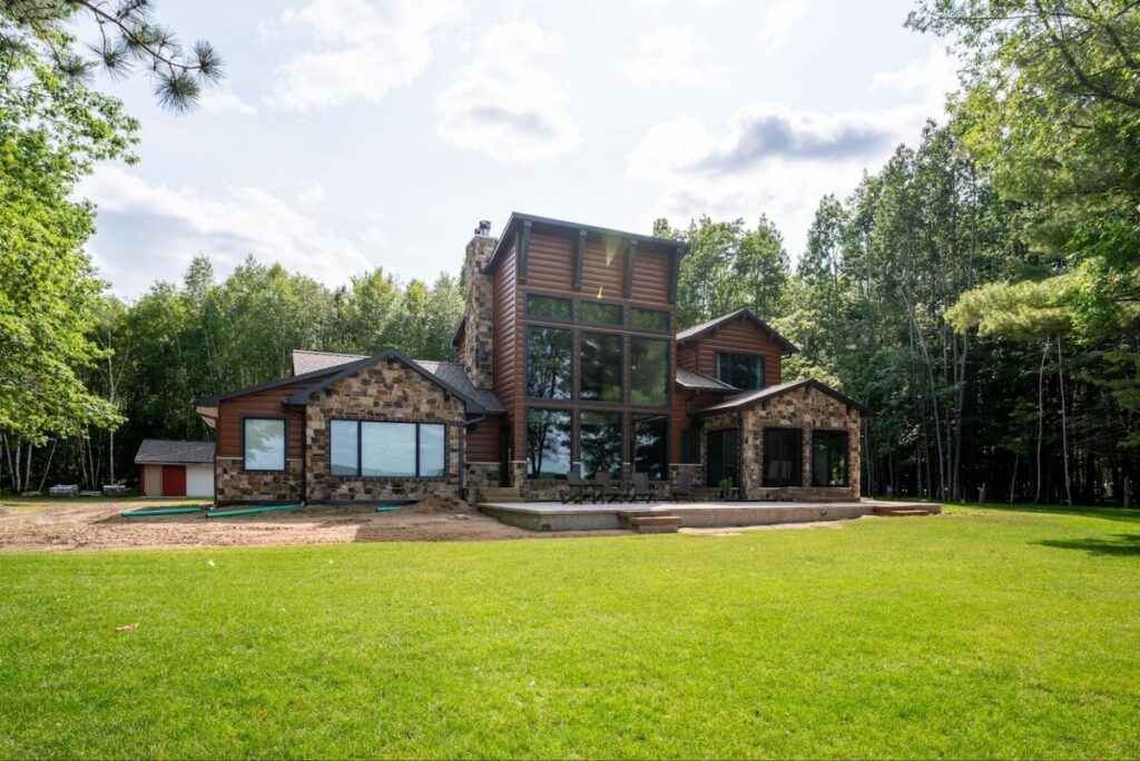 A modern home featuring large windows, stone accents, and TruLog steel log siding