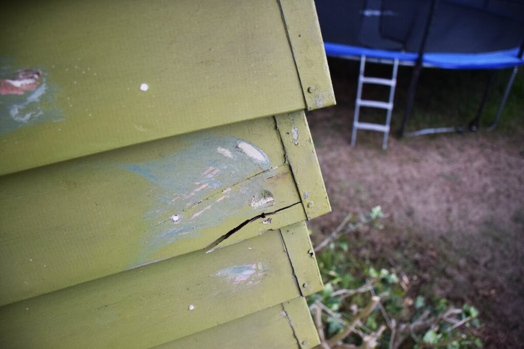 Cracked and damaged wood siding that shows why natural wood isn't the best siding for cold climates.