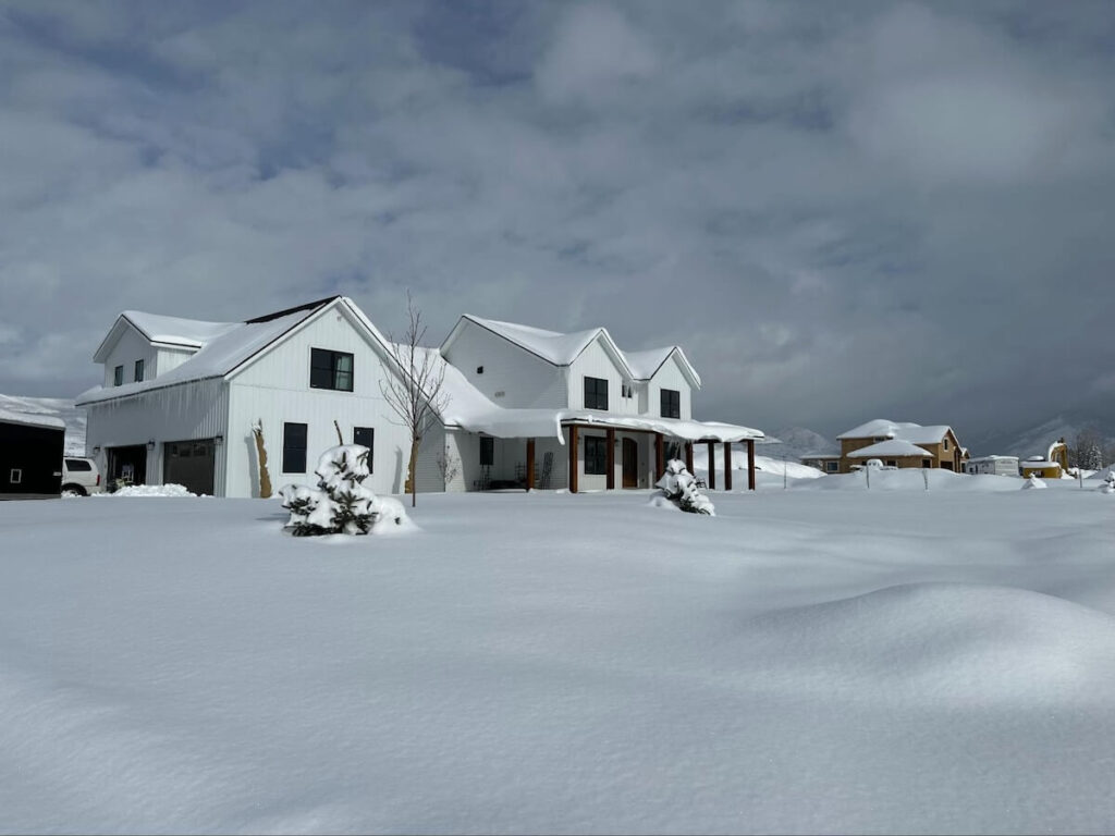 A modern farmhouse with matte white TruLog steel board and batten siding in a snowy landscape