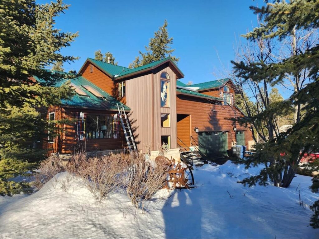 A home with TruLog steel log siding and a green metal roof surrounded by snow, showing energy-efficient exterior design