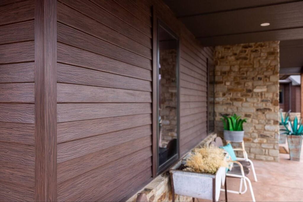 A close-up view of a home exterior featuring TruLog steel lap siding in a rich Dark Walnut finish