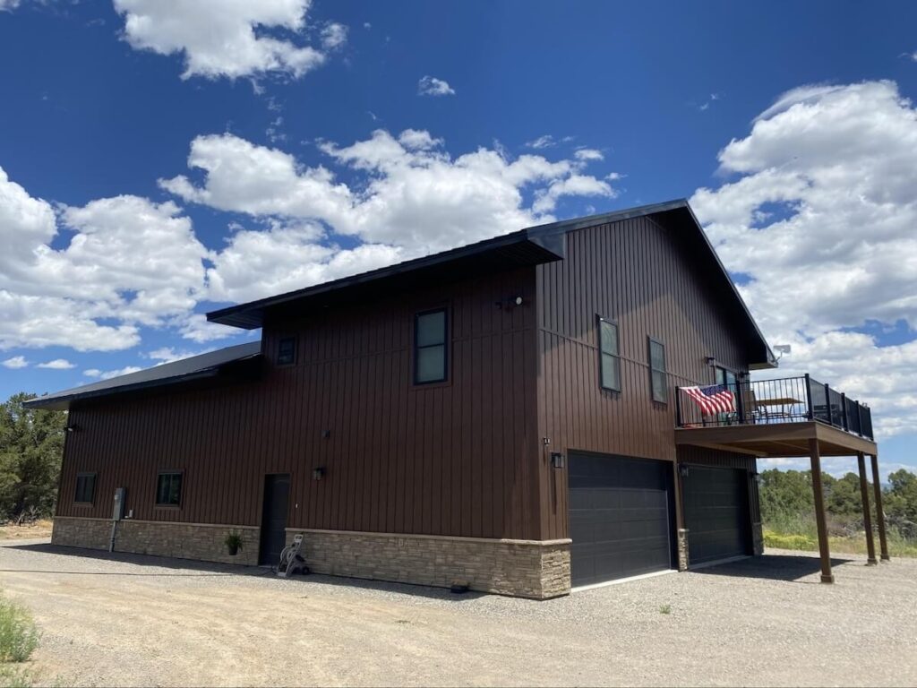 A barndominium with stone around the foundation and TruLog steel board and batten siding