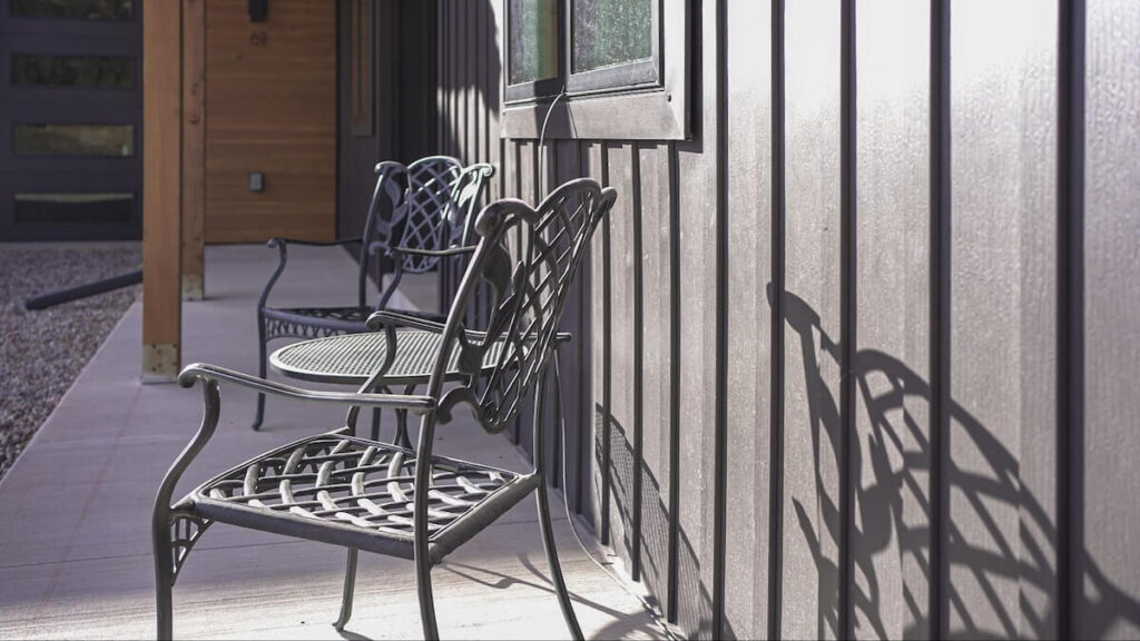 Patio chairs on a concrete patio next to a home with TruLog steel board and batten siding