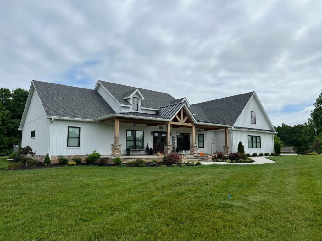 A newly-built home with white siding, timber porch beams, and a wide front lawn