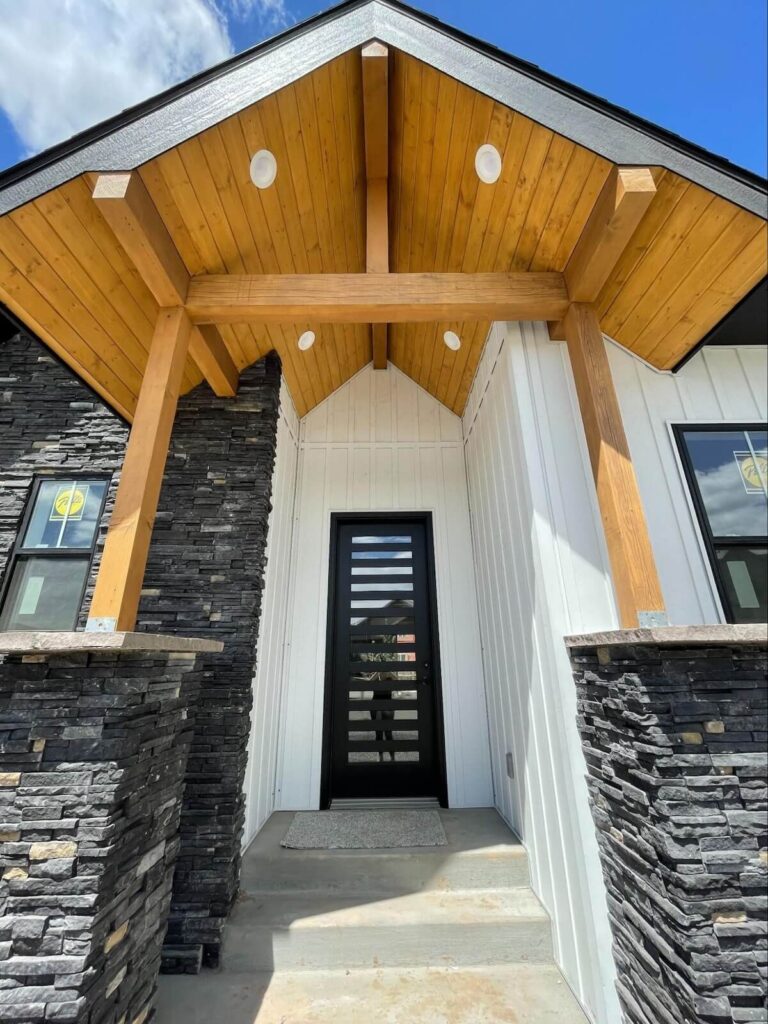 Home entryway with wood beam gabled porch, black front door, and stone accent columns.