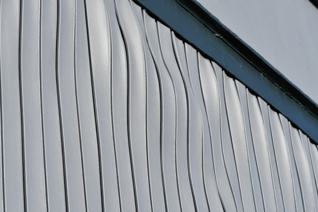 Close-up of gray vinyl siding panels showing severe waviness, distortion, and warping.