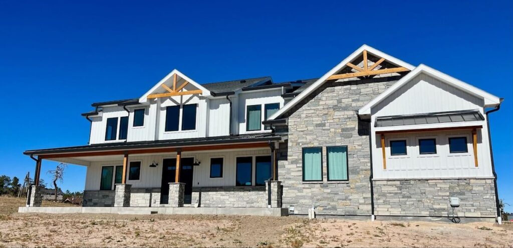 Two-story home with white steel siding and gray stone accents against a clear blue sky.