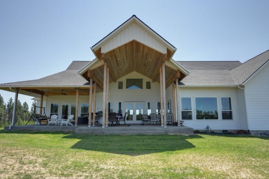 Large modern farmhouse with white TruLog siding and natural wood accents on the gable, featuring a covered porch with outdoor seating.