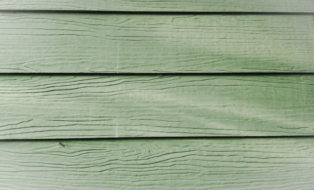 Close-up image of green fiber cement siding with wood grain texture.