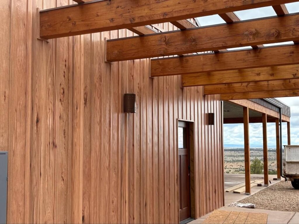 Close-up of TruLog steel siding with a natural wood-look finish on a modern home, with vertical panels and an overhanging beam patio.