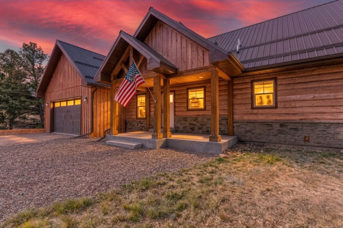 Cabin-style home with TruLog steel log siding, stone wainscoting, and timber porch columns at sunset