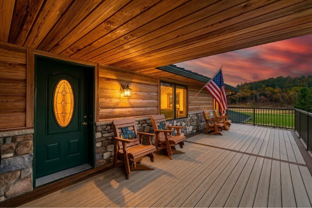 Covered porch of a home with TruLog steel log siding, stone accents, and a sunset view over rolling wooded hills.