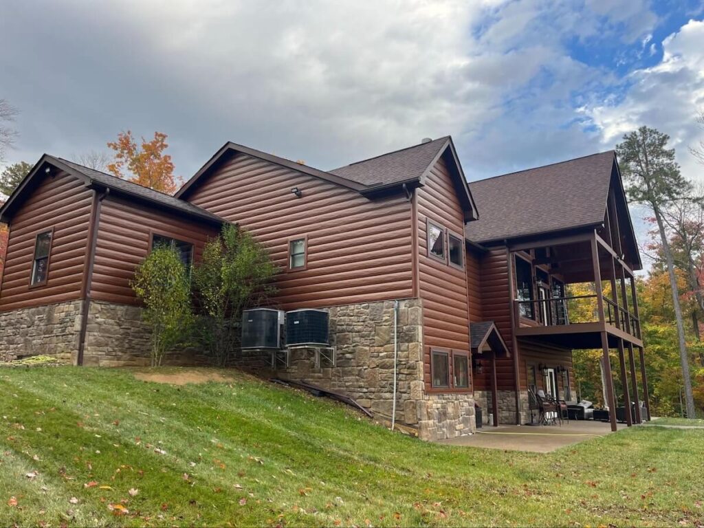 Large cabin with TruLog steel siding, a stone foundation, multiple gables, and a covered lower deck in an autumn setting.