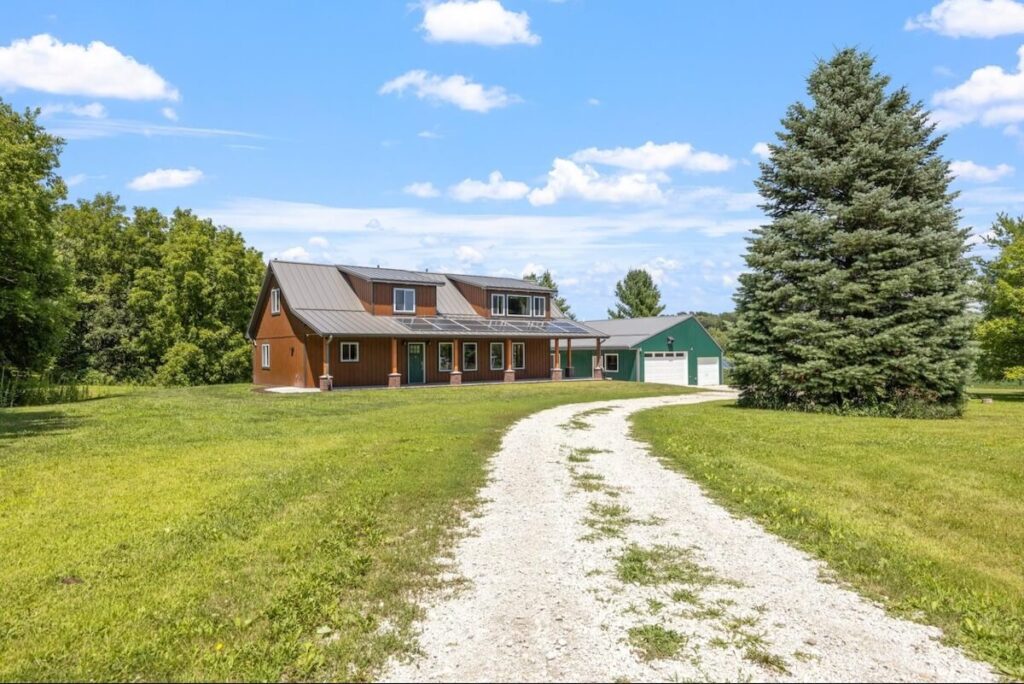 Cabin with TruLog steel siding, a metal roof, and a gravel driveway surrounded by green lawn and trees.