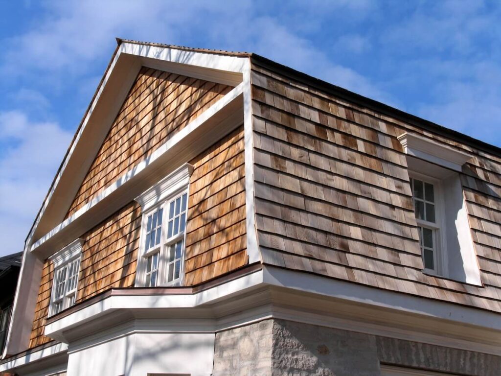 Exterior of a house clad in natural weathered cedar shake siding against a blue sky.