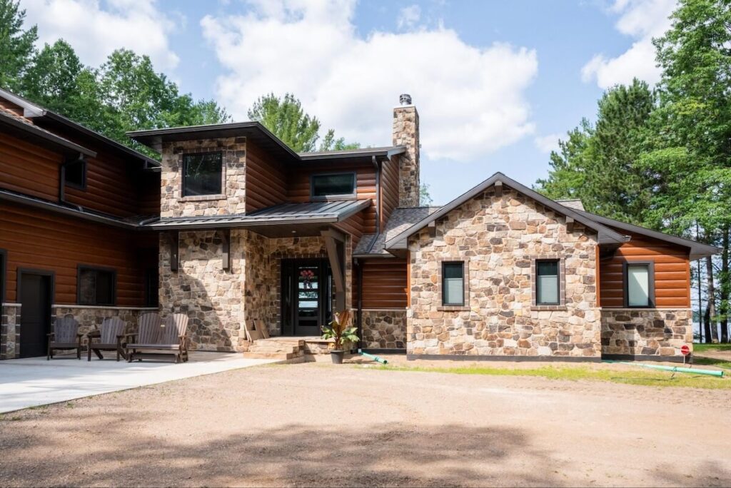 Rustic home exterior featuring log-style siding and natural stone facade with a covered entrance surrounded by pine trees.