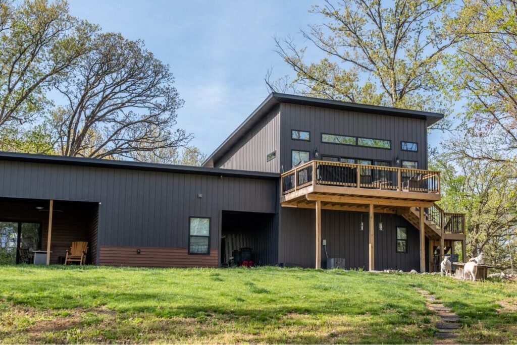Contemporary home with a dark charcoal TruLog steel board and batten exterior, a sloped roofline, and an elevated wood deck on a sunny day.
