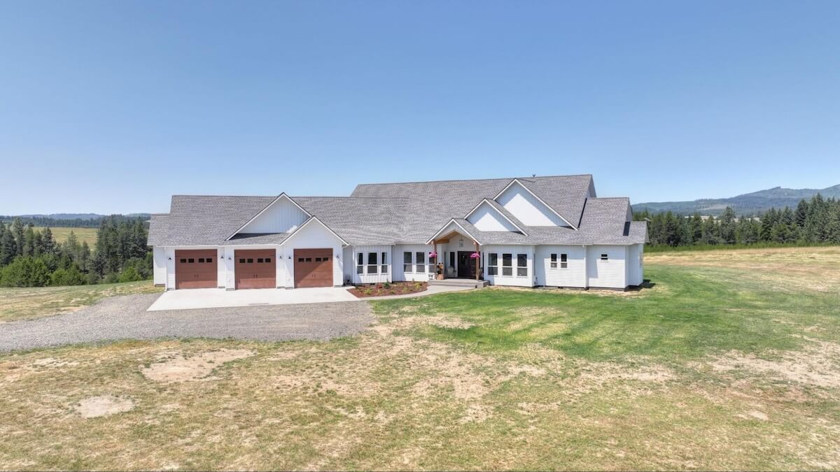 Large ranch-style home with white TruLog steel siding, a three-car garage, and mountain views in the background.